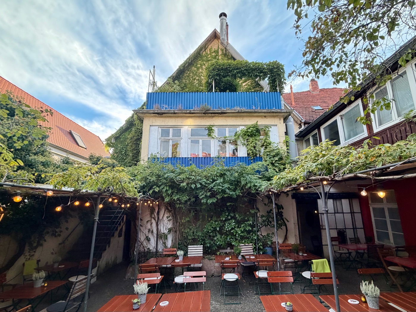 Blick aus dem Hof auf das begrünte Gasthaus mit blauem Balkon